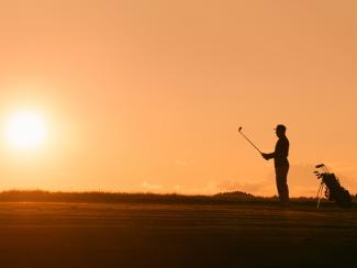 Sun setting as a golfer prepares for a shot on a golf course